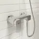 Brausearmatur aus Chrom mit einem einstellbaren Hebel in der Mitte und einem Schlauchanschluss, montiert an einer hellen Kachelwand, von der Marke Ideal Standard.